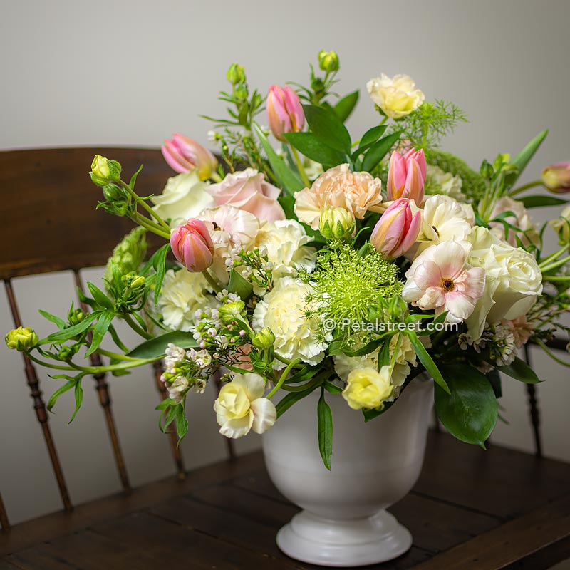 An elegant flower arrangement of pink and white roses, Tulips, Ranunculus, Lace Flower, Carnations, and accent greenery in a compote container by Petal Street Flower Company florist in Point Pleasant, NJ